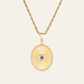 Gold necklace with a oval pendant featuring a blue gemstone on a beige background. This is the evil eye necklace. the Evil Eye wards off negativity while inviting clarity, balance, and good fortune.