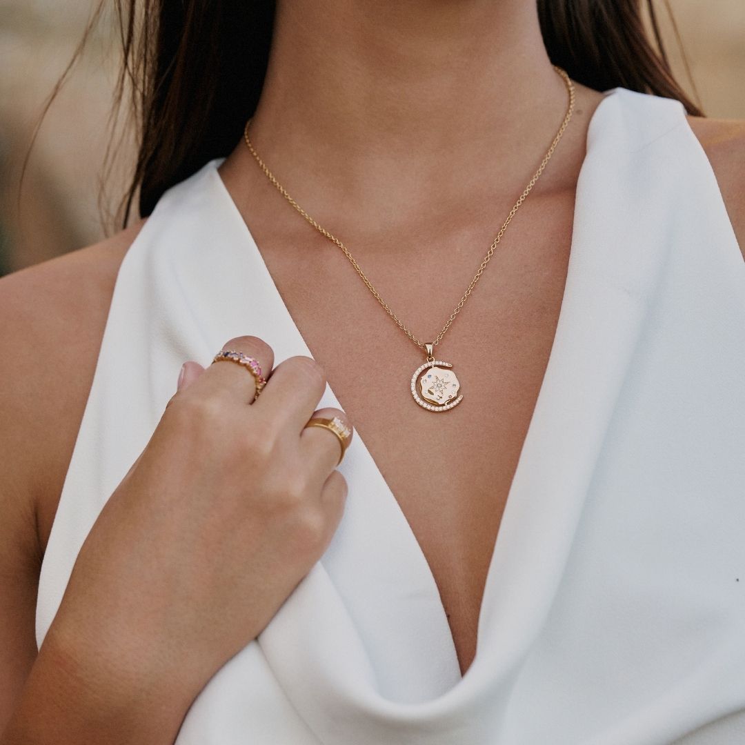 Close-up of a person wearing a gold necklace and rings on a blurred background